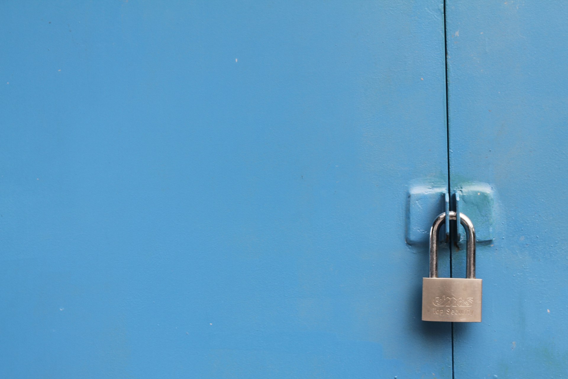 A small silver padlock on a plain blue door.