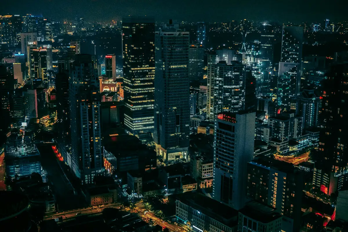A city at night from above, its office towers lit window by window.