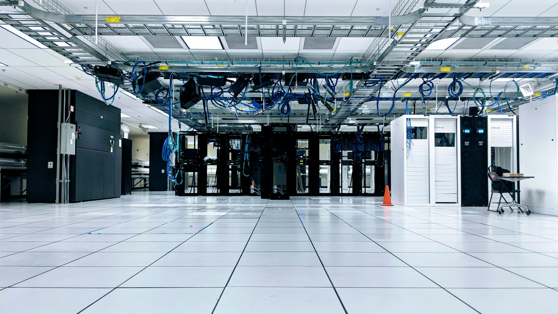 An empty data-center floor with server cabinets and blue cabling overhead.